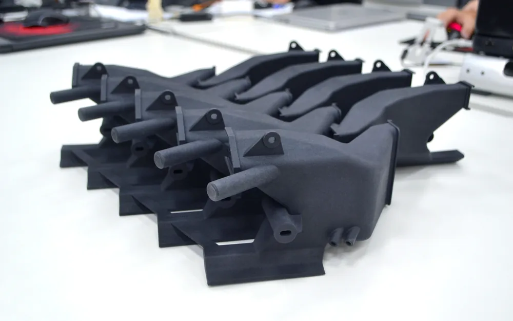 Fekete MJF nylon 3D nyomtatott szívócsonk-prototípusok sorban egy asztalon